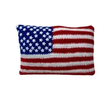 A rectangular cushion designed to resemble the American flag. The top left corner is blue with white stars, and the rest of the cushion is made up of red and white horizontal stripes. The cushion appears to be knitted or crocheted.