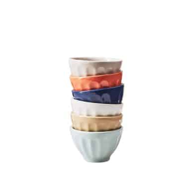 A stack of six small, fluted ceramic bowls in various colors. The bowls are stacked neatly, with colors from top to bottom: white, orange, blue, beige, yellow, and light blue. The background is plain white.