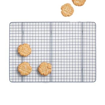 A rectangular wire cooling rack holds four peanut butter cookies topped with a crisscross fork pattern. Three cookies are on the lower left section, and one cookie is near the top right corner. A fifth cookie partially appears off the top edge of the image.