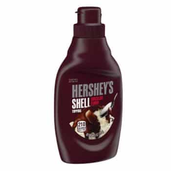 A bottle of Hershey's Shell Chocolate Flavor Topping. The bottle is dark brown with a twist cap and features an image of chocolate being poured over ice cream. The label indicates 210 calories per serving.