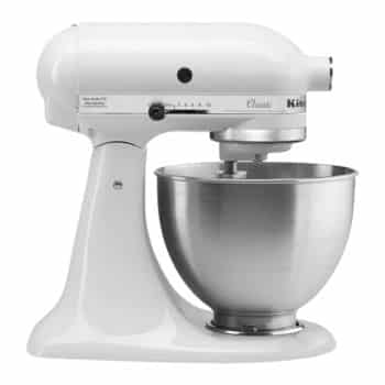A white KitchenAid stand mixer with a metal mixing bowl attached. The mixer has a smooth, curved design and multiple speed settings indicated on the side.