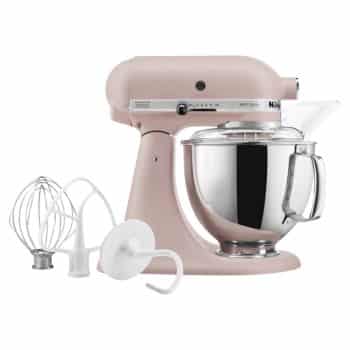 A pink stand mixer with a metal mixing bowl, a pouring shield, and three attachments—a wire whip, a dough hook, and a flat beater—placed next to it. The mixer has multiple speed settings and a tilt-head design.