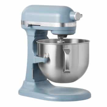 A blue stand mixer with a silver mixing bowl attached, featuring a tilt-head design. The mixer has a sleek, retro appearance with a stainless steel accent band and a beater attachment installed. The brand label is visible on the head of the mixer.