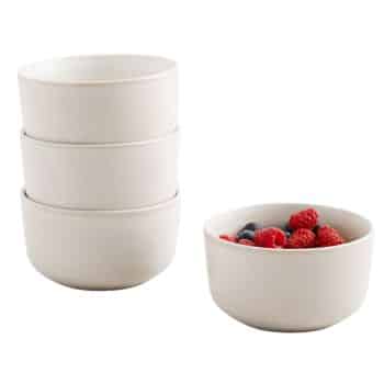 Four white ceramic bowls are shown, three stacked on the left and one on the right filled with raspberries and blueberries.