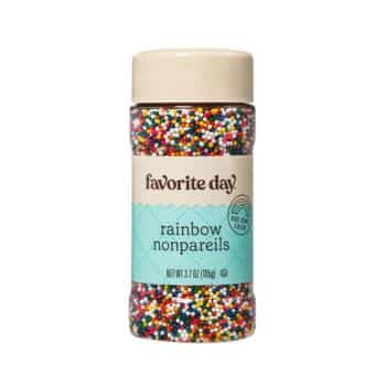 A plastic bottle of "Favorite Day" brand rainbow nonpareils. The label features a teal and cream color scheme with a rainbow icon, and indicates a net weight of 3.7 oz (105g). The bottle is filled with small, colorful round sprinkles.
