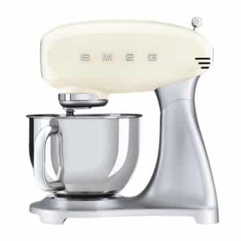 A cream-colored stand mixer with "SMEG" written on the front in silver letters. The mixer has a shiny, metallic mixing bowl attached, supported by a silver base. The design is sleek and modern.