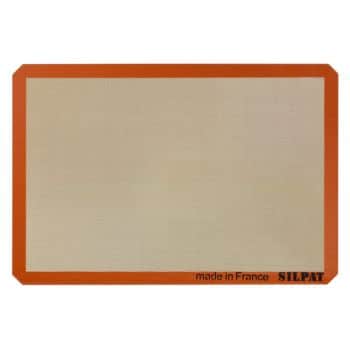 A rectangular, non-stick baking mat with a beige center and an orange border. The bottom right corner has the text "made in France" and "SILPAT" printed in black.
