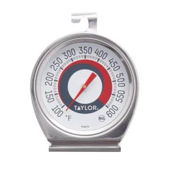 A silver Taylor oven thermometer with black, red, and white markings, showing temperatures from 100°F to 600°F. It has a hook on top for hanging and a flat base for standing upright. .
