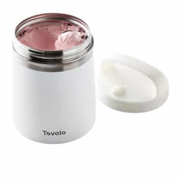 A white Tovolo insulated food container with an open lid sits on a plain background. The container is filled with pink ice cream. The lid, placed beside the container, features subtle ridges and a rotating inner cover for sealing.