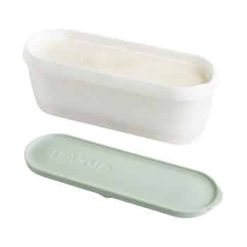 A white rectangular container filled with a light-colored substance, possibly ice cream or batter, beside its matching light green lid labeled "Tovolo." The lid is placed on its side, showing the brand name clearly.