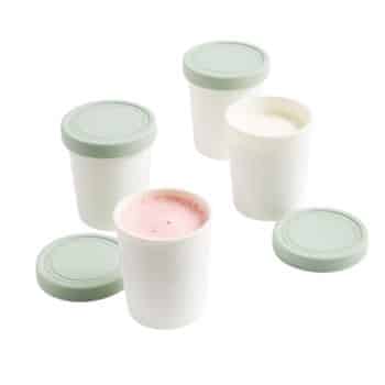 Several white containers with light green lids, some open, revealing different-colored contents. One container has a pink substance inside, another appears to contain a white substance. The lids are placed next to some containers.
