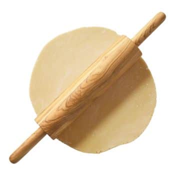 A wooden rolling pin is positioned on top of a piece of rolled-out dough. The rolling pin has a smooth, polished surface, and the dough is spread into a rough circular shape beneath it.