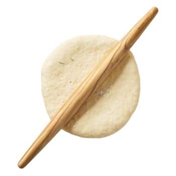 A wooden rolling pin rests diagonally on a round piece of dough. The dough appears to be in the process of being rolled out on a flat surface. The rolling pin has a light, natural wood grain finish.