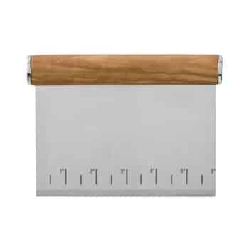 A metal dough scraper with a rectangular stainless steel blade and a wooden handle. The blade features engraved measurements marked in inches along the bottom edge.