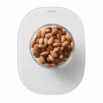 A bowl filled with almonds is placed on a digital kitchen scale. The scale has a white surface and shows a reading of 0.0 grams on its digital display. The brand name "Zwilling" is visible at the top of the scale.