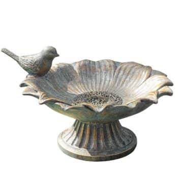 A decorative bird bath made of weathered metal, featuring a flower-shaped basin and a small bird figurine perched on the edge. Elevated on a fluted pedestal, it exudes rustic, vintage charm—perfect for enhancing your flower garden decor ideas and more.