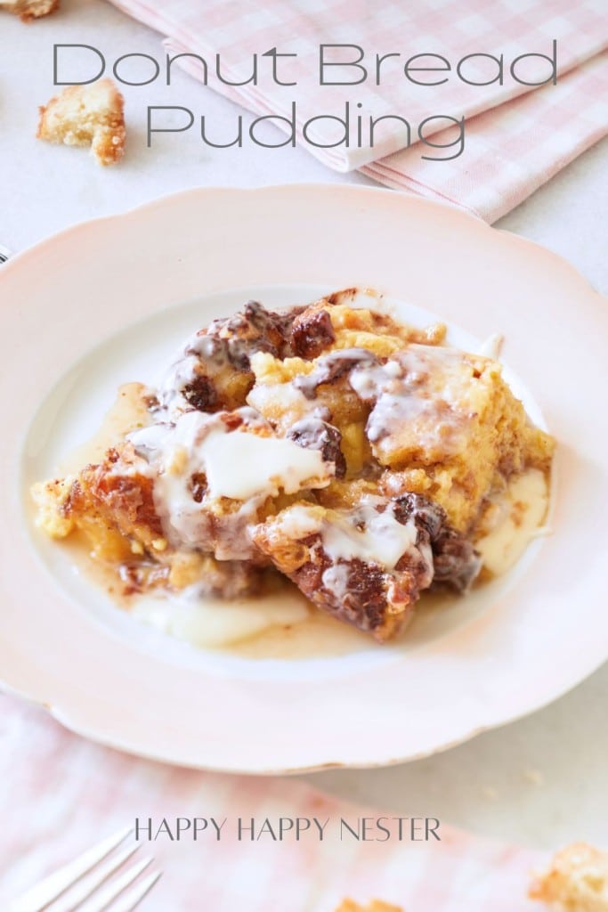 A dessert plate on a light pink tablecloth holds a serving of donut bread pudding topped with glaze. Text on the image reads "Donut Bread Pudding" and "HAPPY HAPPY NESTER." Crumbs and a partially visible napkin are in the background.