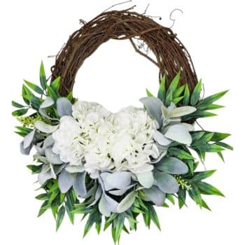 A decorative wreath made of intertwined brown branches is adorned with large white hydrangeas and surrounded by a mix of green and grayish-green leaves. The arrangement has a natural, elegant look, suitable for various occasions or home decor.