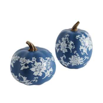 Two decorative pumpkins painted in a matte blue finish and adorned with delicate white floral patterns. The pumpkins' stems are brown, and the intricate designs give them an elegant and stylish appearance. They are positioned against a plain white background.