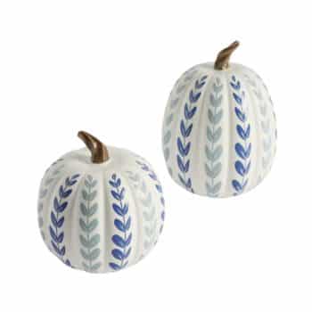 Two decorative white ceramic pumpkins with vertical leaf patterns. The leaves are painted in alternating shades of blue and teal, and each pumpkin features a small, gold-colored stem on top. These ornaments are arranged in a simple, clean style.