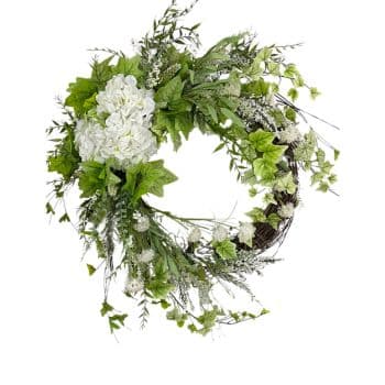 A lush, circular wreath composed of green leaves, white flowers, and delicate sprigs of greenery. The foliage is arranged in a balanced manner, creating a fresh and natural look. The wreath is on a white background.
