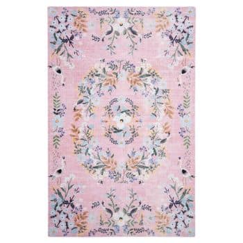 A rectangular pink rug with a vintage floral pattern. The design features an oval-shaped arrangement of flowers in pastel colors, surrounded by smaller floral patterns. The rug has a faded, antique appearance with a blend of pale pink, lavender, yellow, and green hues.