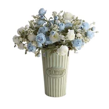 A light green vase with vertical ridges and the word "GARDEN" embossed on it holds an arrangement of blue, white, and ivory artificial flowers. The bouquet appears lush and is composed of small, delicate blossoms and green leaves.