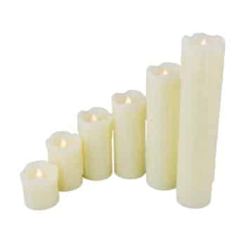 A row of six white pillar candles of varying heights, each lit with a small flame. The candles range from short to tall, arranged in ascending order from left to right. The tallest candle is on the far right, and the shortest is on the far left.