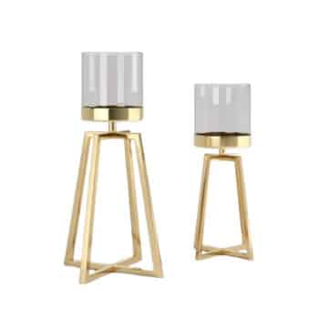 Two modern candle holders with gold geometric frames and cylindrical glass covers. The holders are of different heights, with the taller one on the left and the shorter one on the right. The design is sleek and contemporary.