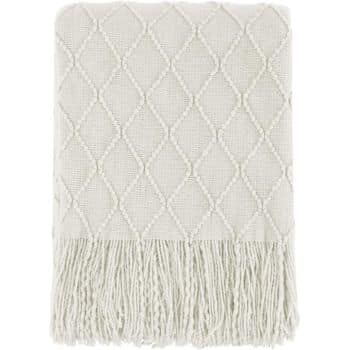 A folded light-colored throw blanket with a diamond pattern and fringe detailing on the edge. The texture appears soft and cozy, suitable for use as a decorative or functional piece in a living space.