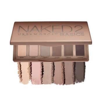 An open Urban Decay Naked2 Basics eyeshadow palette displaying six neutral shades. The shades are swatched below the palette from left to right: a light cream, a beige, a taupe, a soft brown, a dark brown, and a deep grayish-brown.