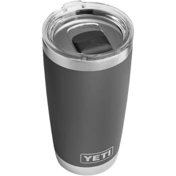 A gray and stainless steel YETI tumbler with a clear, plastic lid. The cup is cylindrical with a latching mechanism on the lid for opening and closing. The YETI logo is visible near the bottom of the tumbler.