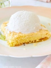 A slice of yellow cake topped with a scoop of vanilla ice cream is served on a pastel-colored plate. In the background, a pink and white striped napkin and a glass vase with flowers are partially visible. The text "HAPPY HAPPY NESTER" appears at the bottom.