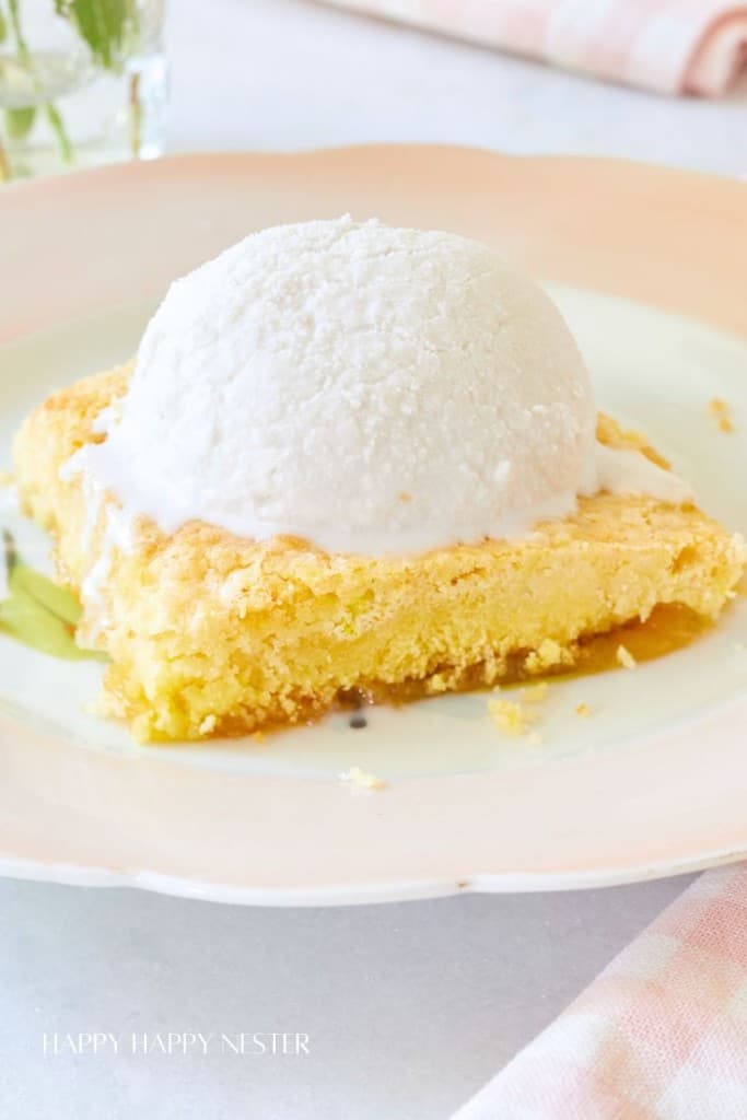 A slice of yellow cake topped with a scoop of vanilla ice cream is served on a pastel-colored plate. In the background, a pink and white striped napkin and a glass vase with flowers are partially visible. The text "HAPPY HAPPY NESTER" appears at the bottom.