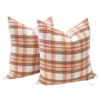 Two decorative square pillows with a plaid pattern in shades of orange, yellow, green, and white. The pillows are positioned upright and slightly tilted against each other, showcasing their vibrant and cozy design.