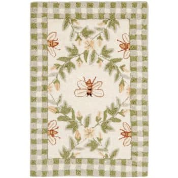 A decorative rectangular rug with a green and white checkered border. The interior features a bee motif surrounded by green leaves and orange flowers, with a central bee design. The overall color scheme includes shades of green, white, and beige.