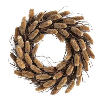 A decorative wreath made of natural materials, featuring tightly packed, elongated seed pods in earthy tones of beige and brown, interwoven with thin, twig-like branches in darker brown. The wreath has a rustic, textured appearance and is circular in shape.