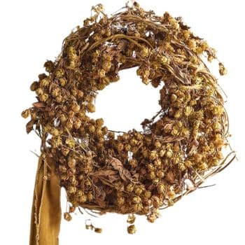 A wreath made of dried yellow flowers and leaves. The flowers are clustered tightly together, creating a rustic and natural look. A piece of brown fabric is hanging from the bottom part of the wreath.