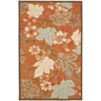 A rectangular rug with an orange background features an intricate floral design. The pattern includes large leaves and blossoms in shades of white, light blue, brown, and red. The rug has a dark brown border.