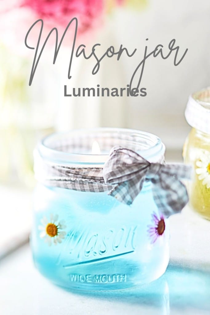 A mason jar luminary with a lit candle inside, decorated with a piece of checkered fabric tied around its neck and small daisy flowers on its surface. The background is softly blurred, and the text "Mason jar Luminaries" is written at the top.