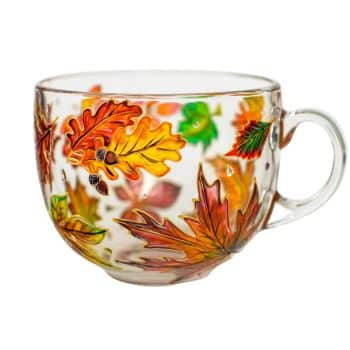 A transparent glass mug decorated with colorful autumn leaves in shades of orange, yellow, green, and red. The leaves are scattered around the exterior, creating a fall-themed design. The mug has a clear handle and is empty.