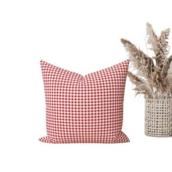 A square throw pillow with a red and white checkered pattern is placed next to a decorative vase filled with dried pampas grass, creating a cozy and rustic aesthetic.