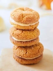 A stack of four sandwich cookies with golden brown, sugar-coated exteriors and a creamy filling in the middle. The cookies are set on a piece of parchment paper with a blurred background.