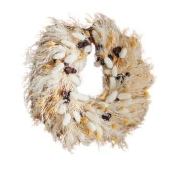 A circular wreath made from dried grasses, seed pods, and white fluffy elements, interspersed with dark brown and yellow accents. The wreath has a rustic and natural appearance, with the materials arranged to create a full and textured look.