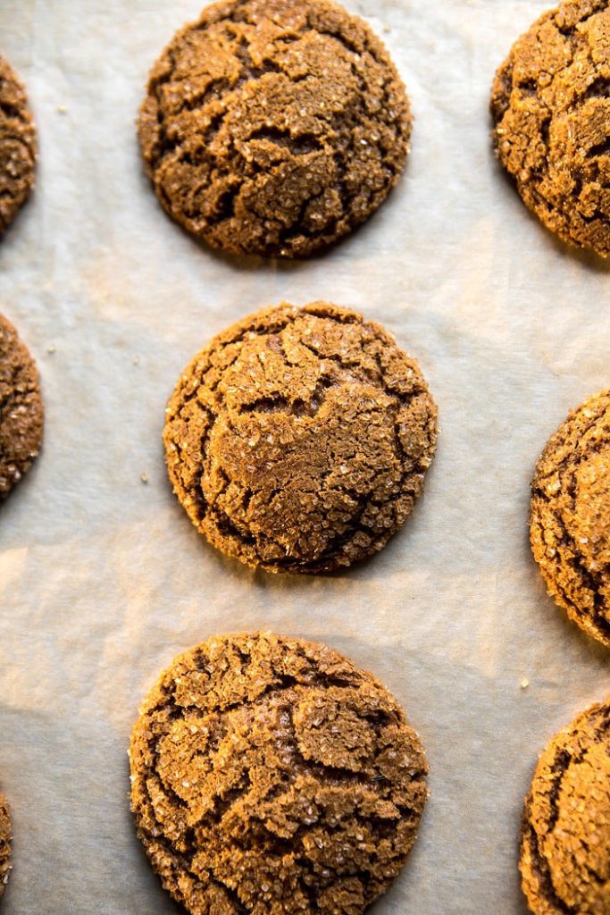 Nine round, cracked fall cookies arranged in rows on a sheet of parchment paper, fresh from baking.