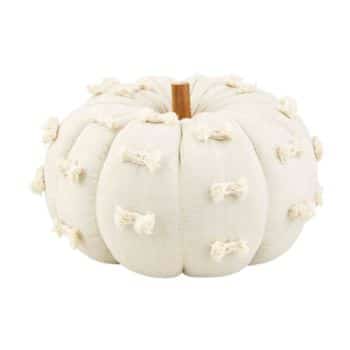 A decorative, white plush pumpkin with a fabric texture is adorned with small, cream-colored bow accents. The pumpkin features a soft, rounded shape and a realistic brown stem, blending a cozy and festive aesthetic.