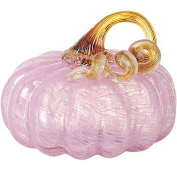 A glass pumpkin with a pale pink body and a golden, curly stem. The pumpkin features a smooth and shiny texture, reflecting light and showcasing intricate details in the glasswork.