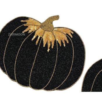 A close-up of a decorative black pumpkin with gold accents. The pumpkin is designed with detailed, intricate beading and stitching, giving it a textured and elegant appearance. The background is plain white.