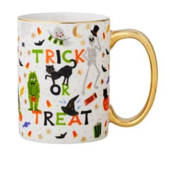 A festive Halloween-themed mug with a gold handle, featuring the phrase "Trick or Treat" in colorful letters. The mug is decorated with various Halloween motifs, including a skeleton, a black cat, a witch hat, candies, bats, and stars.