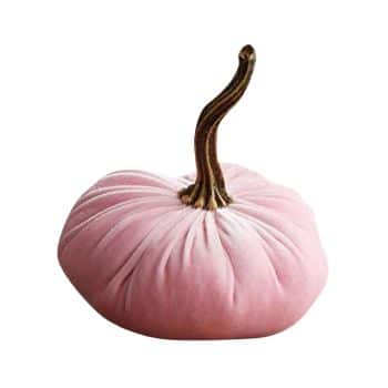 A plush pumpkin decoration with a soft pink, velvety body and a long, slightly curved brown stem. The pumpkin has a smooth, rounded shape with subtle vertical creases.